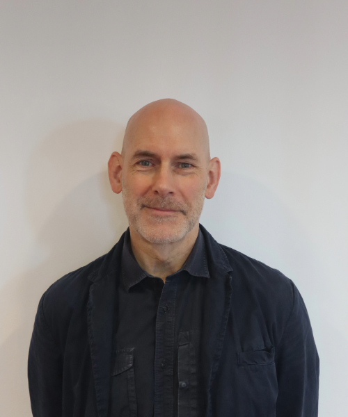 Headshot of Mick Laverty, he is facing the camera and smiling, he wears a navy blue shirt and jacket